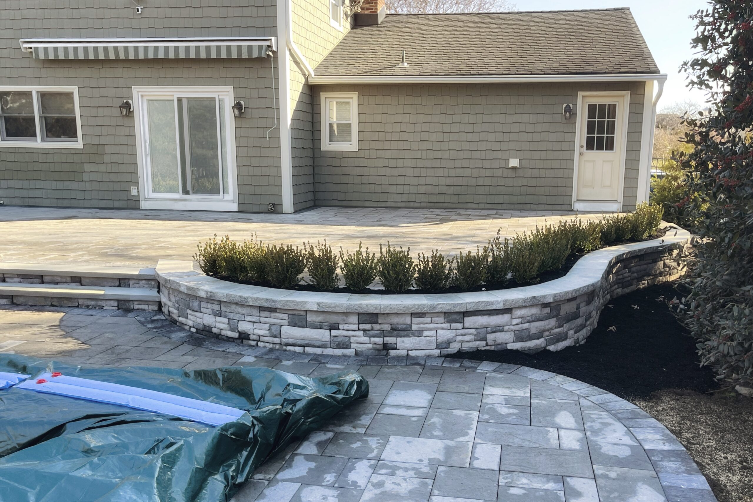 Finished backyard curved stone patio with lined shrubs