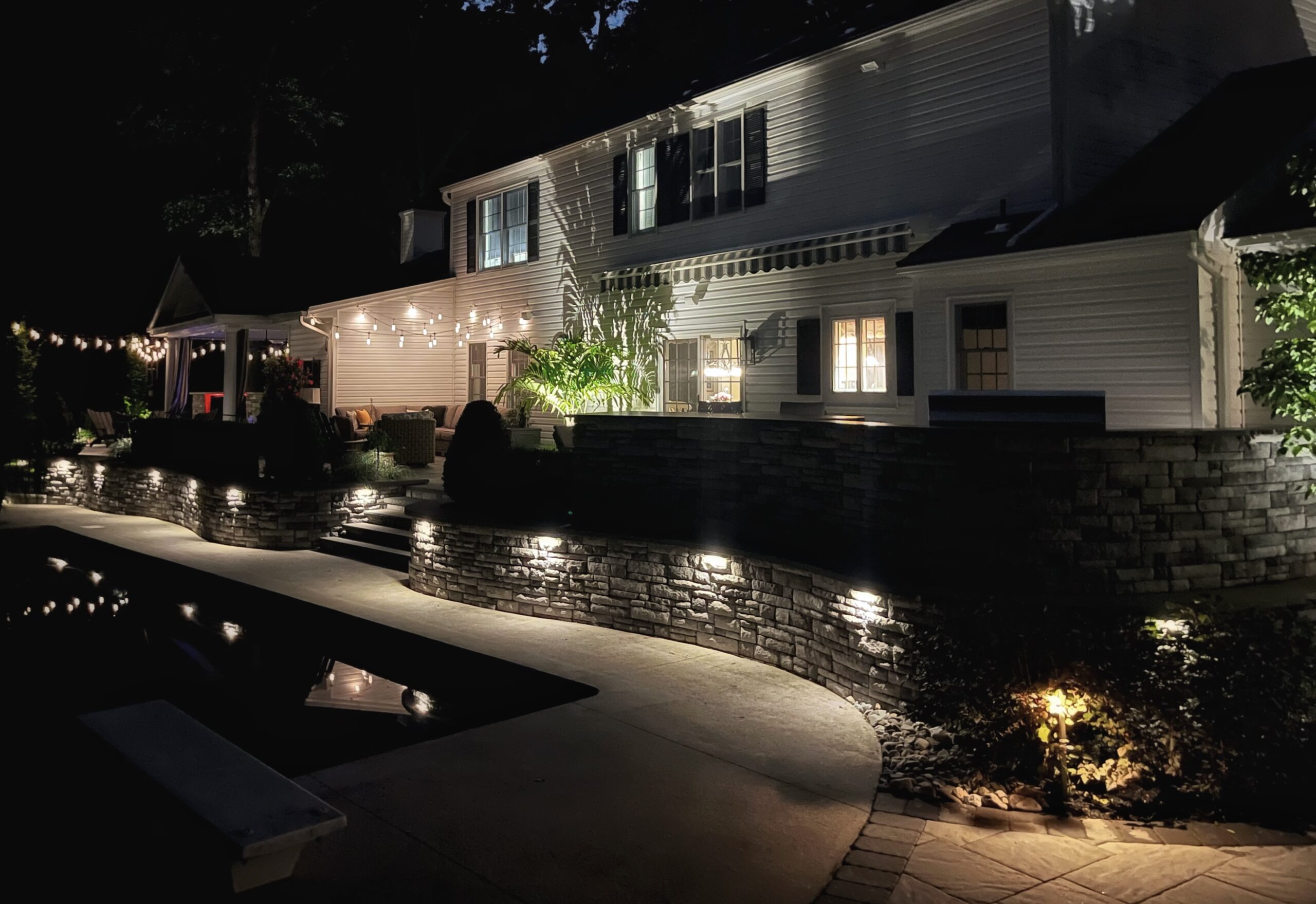 Stone patio at night with landscape lighting installed at residential property in Middletown, NJ.
